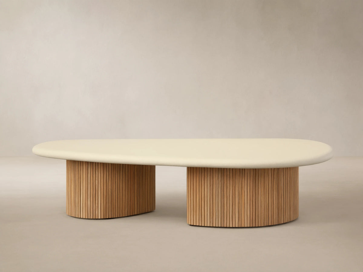 Alesso Outdoor Coffee Table with a light beige oval top and two cylindrical natural wood slatted bases, on a stone patio.