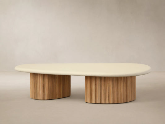 Alesso Outdoor Coffee Table with a light beige oval top and two cylindrical natural wood slatted bases, on a stone patio.