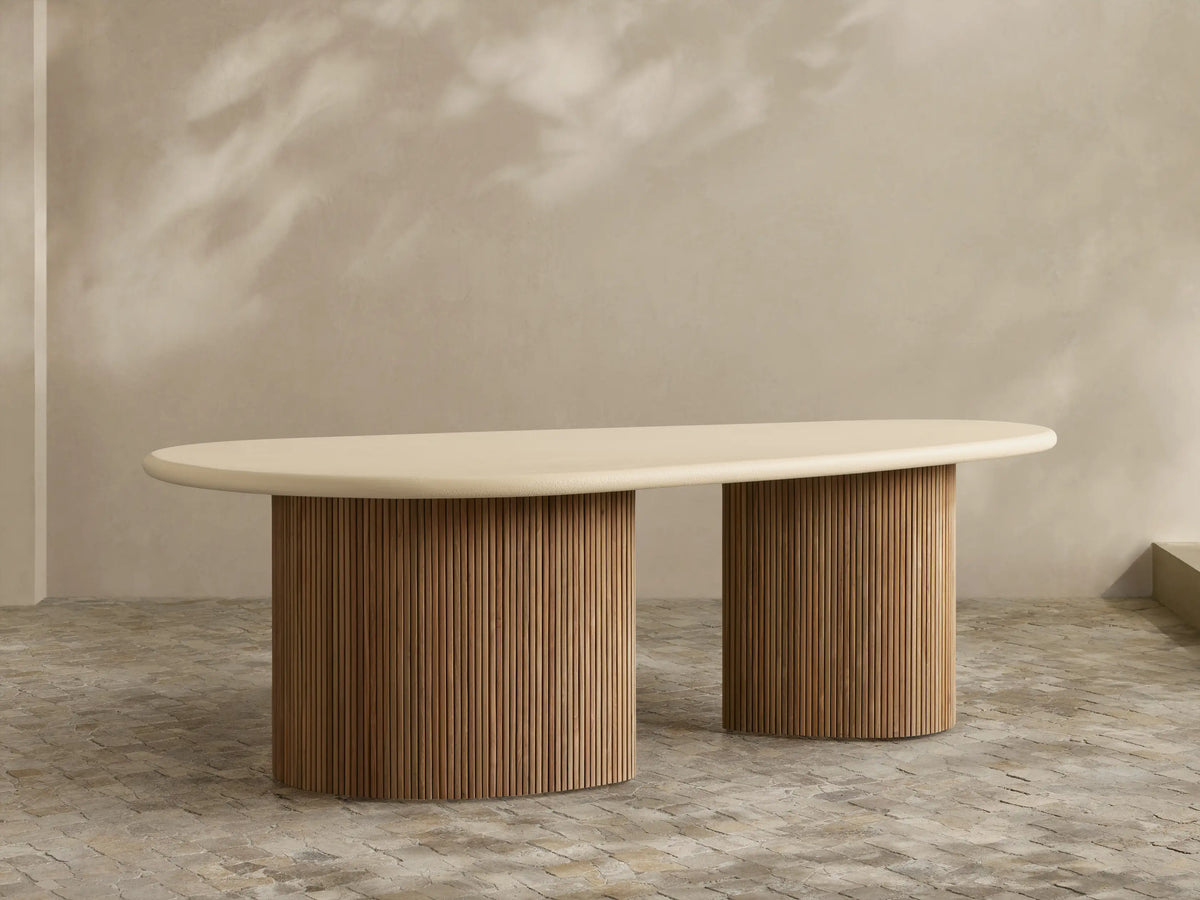 Alesso Outdoor Dining Table, oval light beige top, two natural wood cylindrical bases with vertical ridges on a patio.