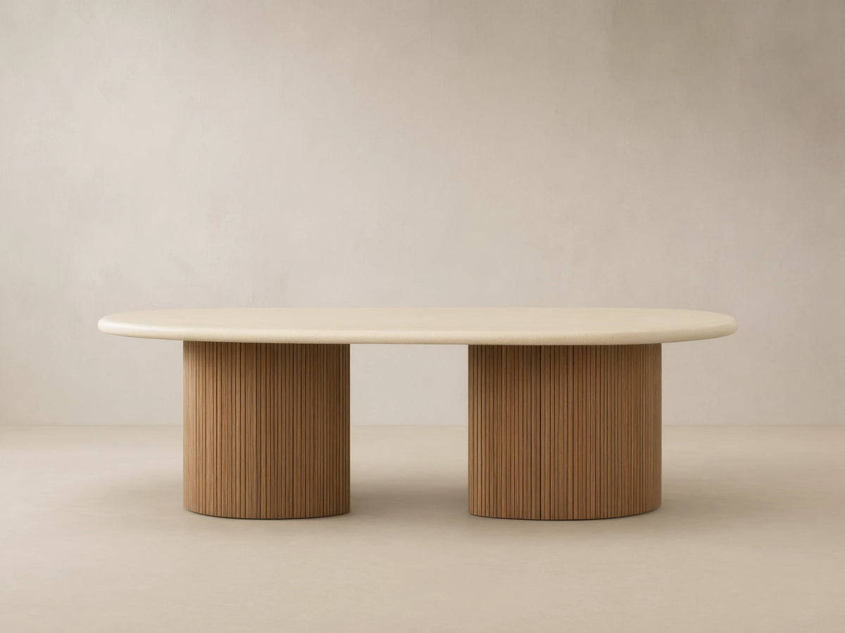 Alesso Outdoor Dining Table, oval light beige top, two natural wood cylindrical bases with vertical ridges on a patio.
