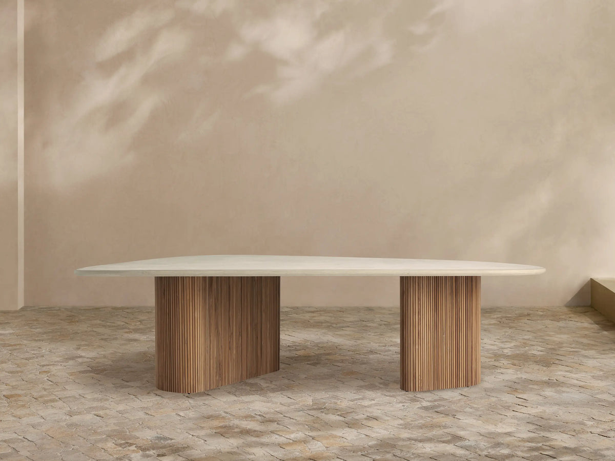 Alesso Outdoor Dining Table with an oval light gray concrete tabletop resting on two fluted natural teak wood bases. Minimalist scene.