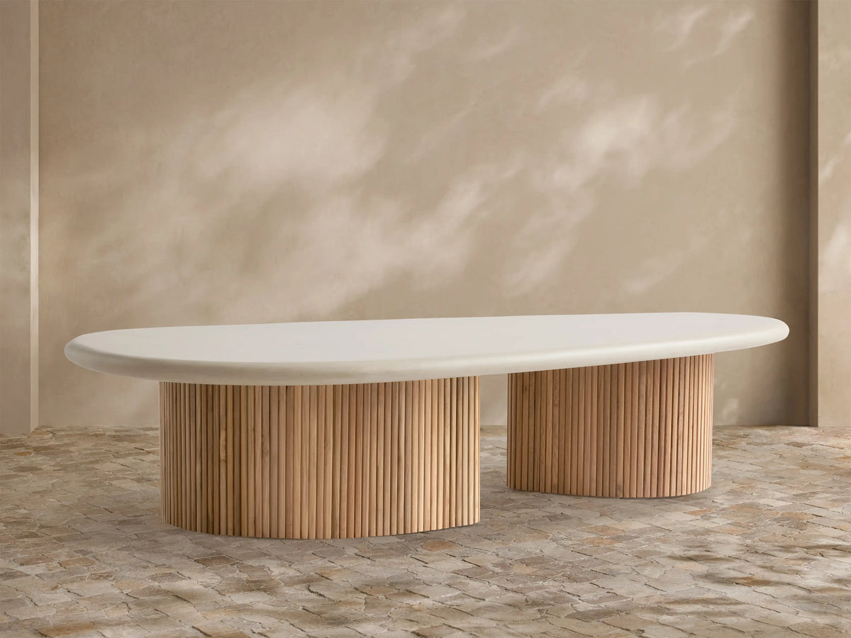 Alesso Outdoor Coffee Table with an oval cream tabletop on two semi-circular slatted natural wood bases, set on a stone patio.