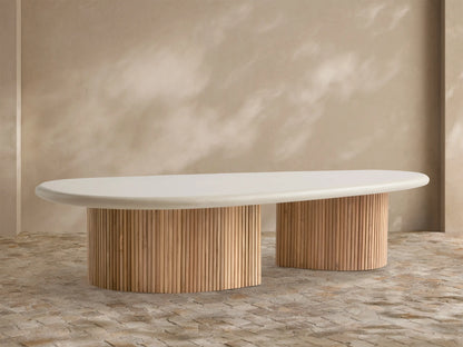 Alesso Outdoor Coffee Table with an oval cream tabletop on two semi-circular slatted natural wood bases, set on a stone patio.