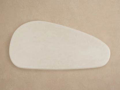 Alesso Outdoor Coffee Table with a light beige oval top and two light natural wood fluted cylindrical legs, against a beige wall.