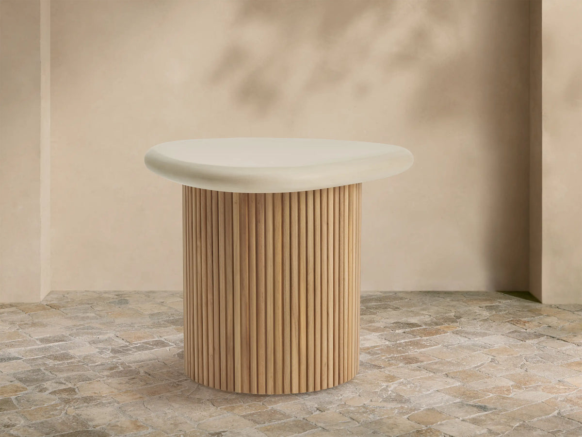 Alesso Outdoor End Table with a cream, organic-shaped top and a slatted natural wood cylindrical base, on a stone patio.