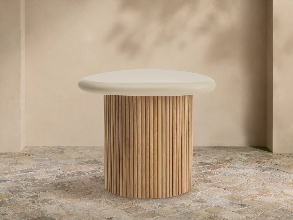 Alesso Outdoor End Table with a cream, organic-shaped top and a slatted natural wood cylindrical base, on a stone patio.