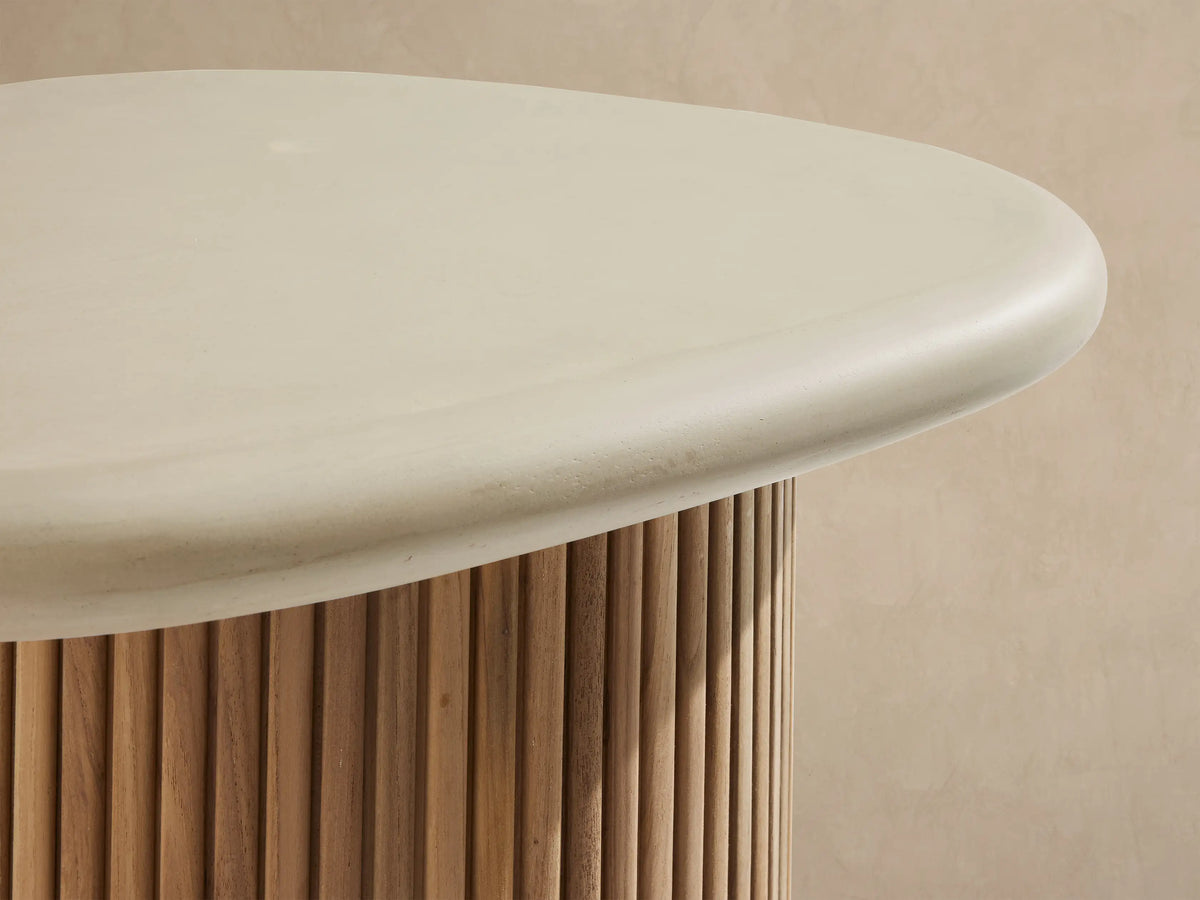 Alesso Outdoor End Table with a light cream rounded oval top and a natural wood slatted cylindrical base on a stone patio.