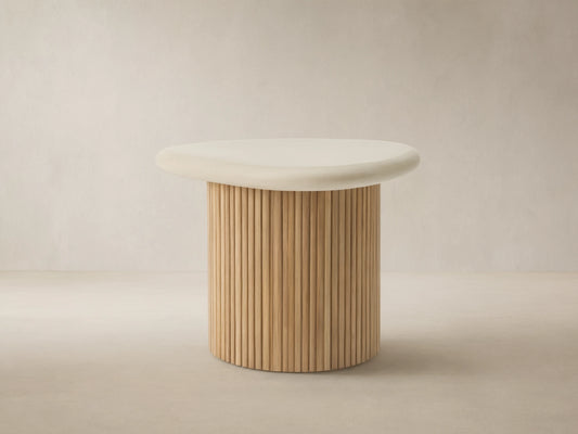 Alesso Outdoor End Table with a cream, organic-shaped top and a slatted natural wood cylindrical base, on a stone patio.