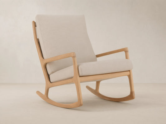 Altea Outdoor Rocking Chair with light teak wood frame and light beige cushions, angled on a stone tile floor.