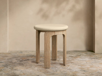 Anami Outdoor End Table with a light, round top and four curved, natural teak wood legs on a tiled floor.