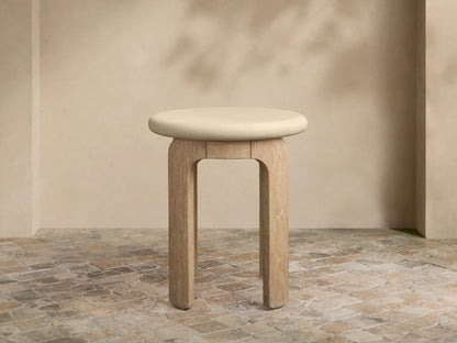 Anami Outdoor End Table with a light, round top and four curved, natural teak wood legs on a tiled floor.