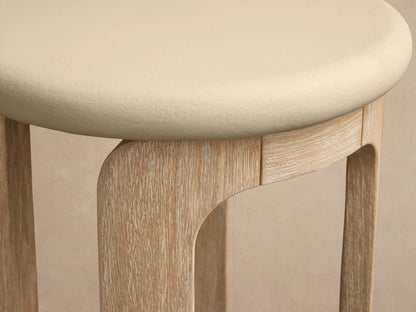 Anami Outdoor End Table: round cream top, light natural teak U-shaped legs on a stone floor, against a beige wall.