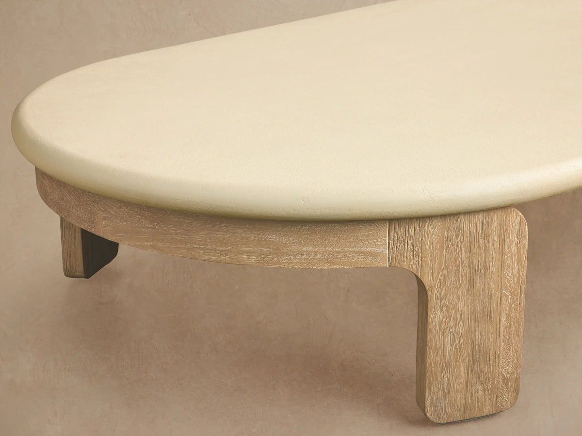 Anami Outdoor Coffee Table: low, oval cream top on light natural teak wood slab legs, on a textured stone patio.