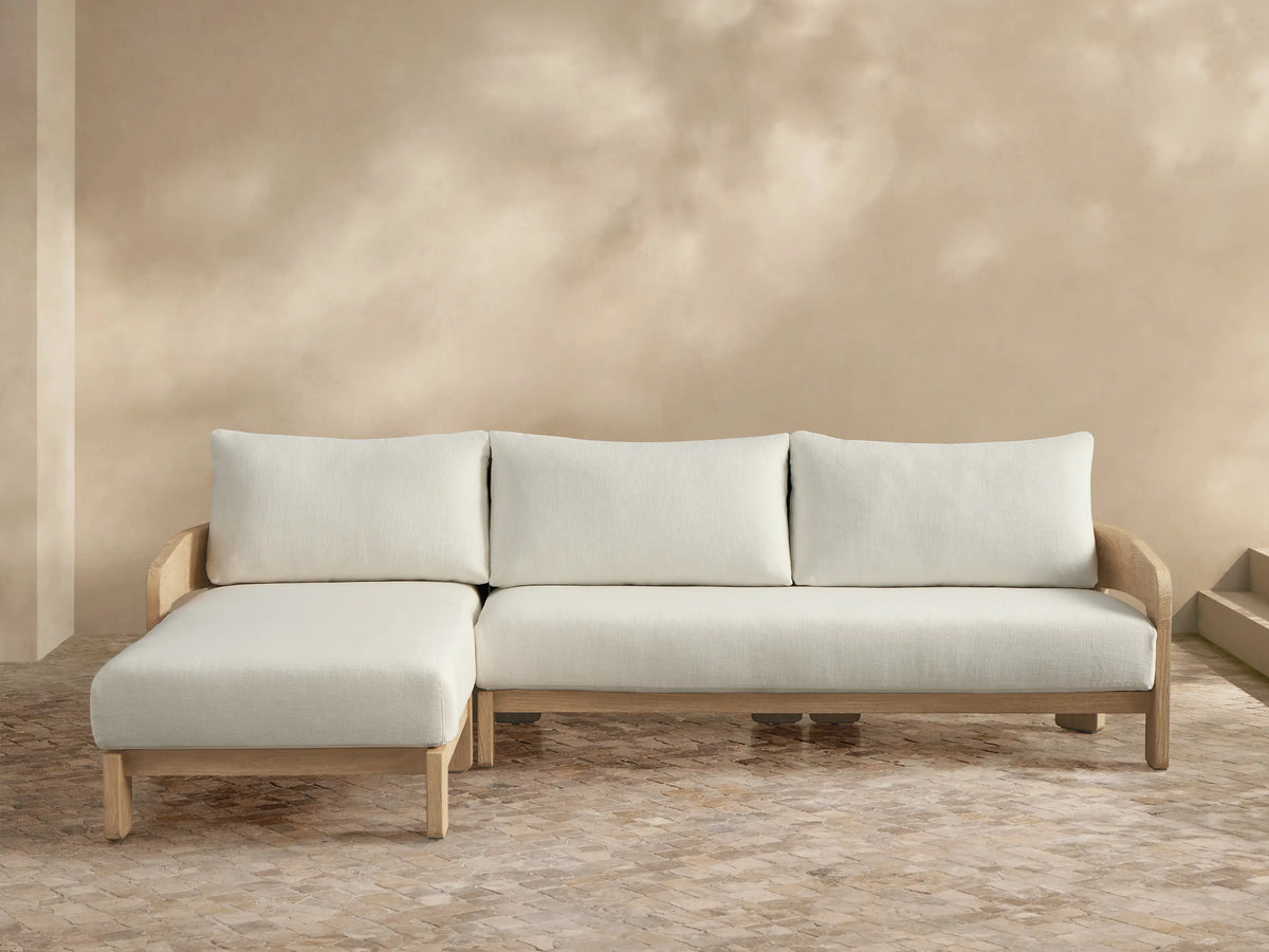 Anami Outdoor Two-Piece Chaise Sectional with light teak frame, plush cream cushions, and left-facing chaise lounge on a tiled patio.