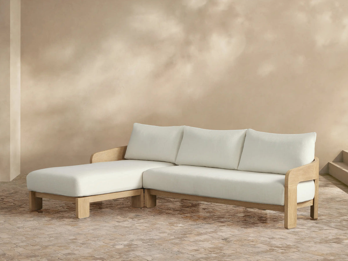 Anami Outdoor Two-Piece Chaise Sectional with light teak frame, plush cream cushions, and left-facing chaise lounge on a tiled patio.