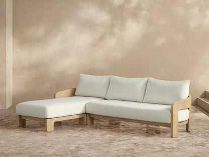 Anami Outdoor Two-Piece Chaise Sectional with light teak frame, plush cream cushions, and left-facing chaise lounge on a tiled patio.
