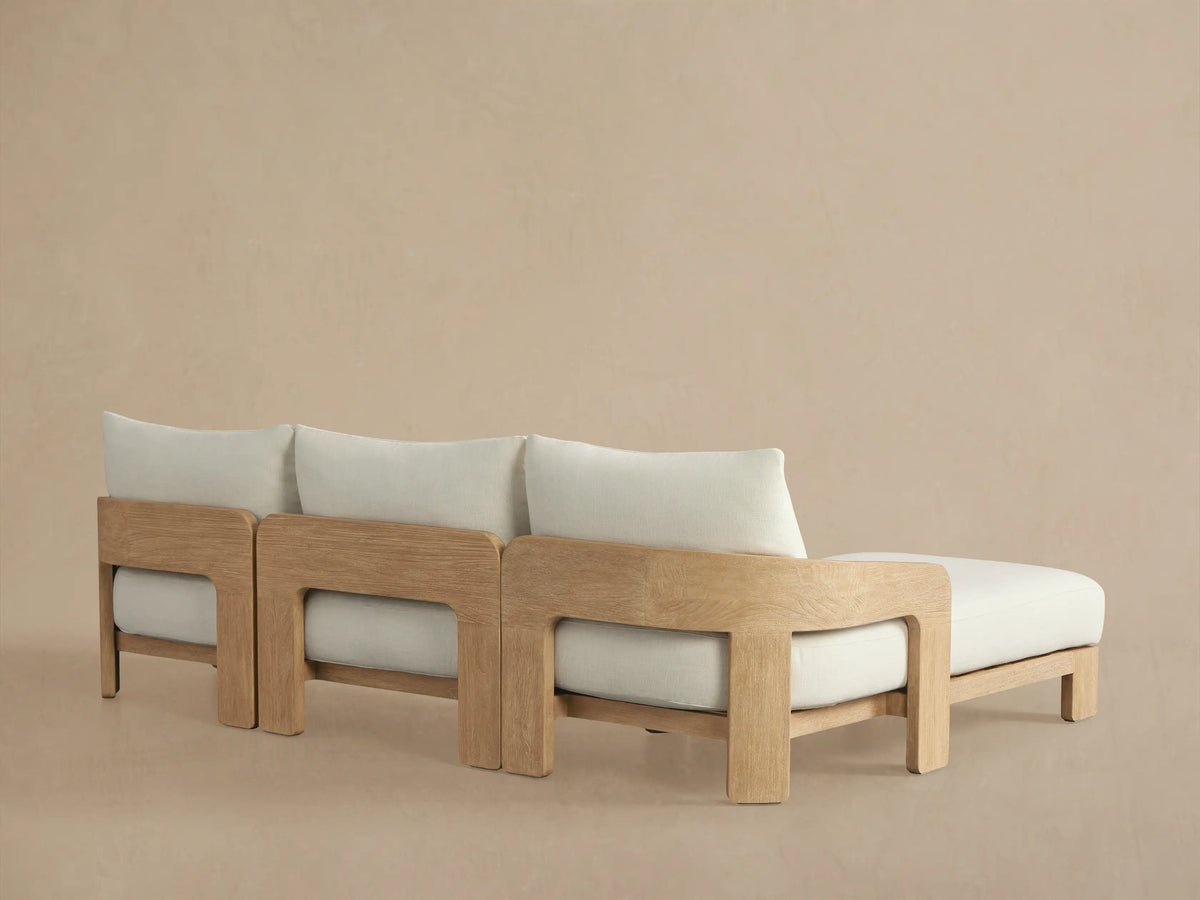 Close-up: Anami Outdoor Chaise Sectional. Distressed light teak wood armrest framing soft cream cushion and back pillow.
