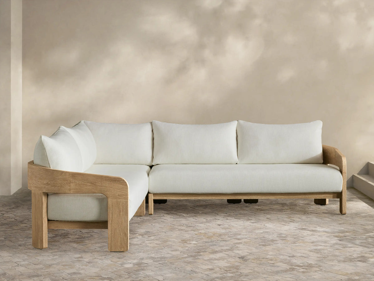 Anami Outdoor Two-Piece L-shaped sectional with light teak wood frame and off-white cushions on a stone patio.