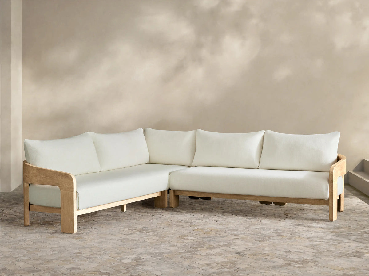 Anami Outdoor Two-Piece L-shaped sectional with light teak wood frame and off-white cushions on a stone patio.