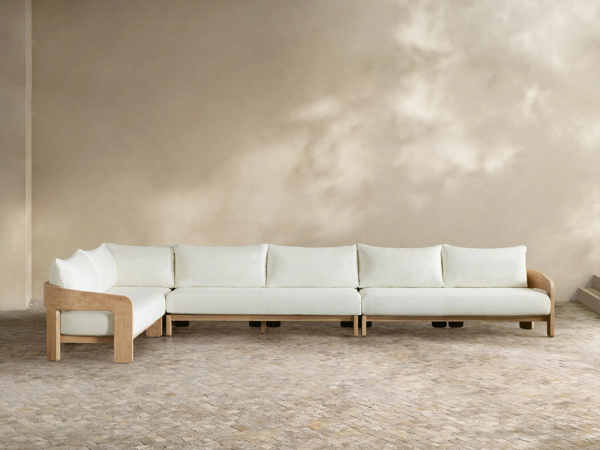 Anami Outdoor L-shaped corner sectional. Light teak wood frame with white cushions. A corner piece & two straight sections on tiled floor.