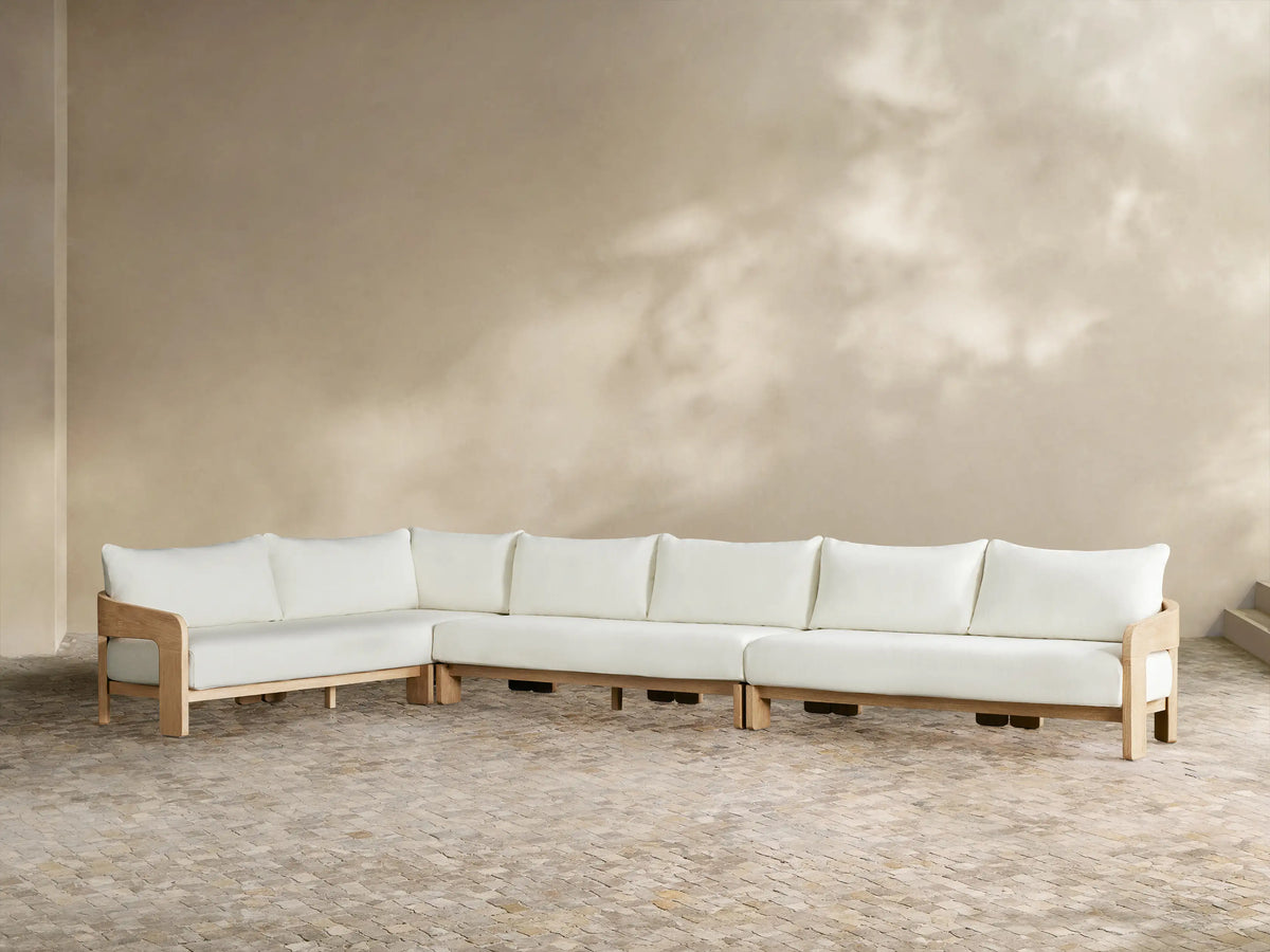Anami Outdoor L-shaped corner sectional. Light teak wood frame with white cushions. A corner piece & two straight sections on tiled floor.