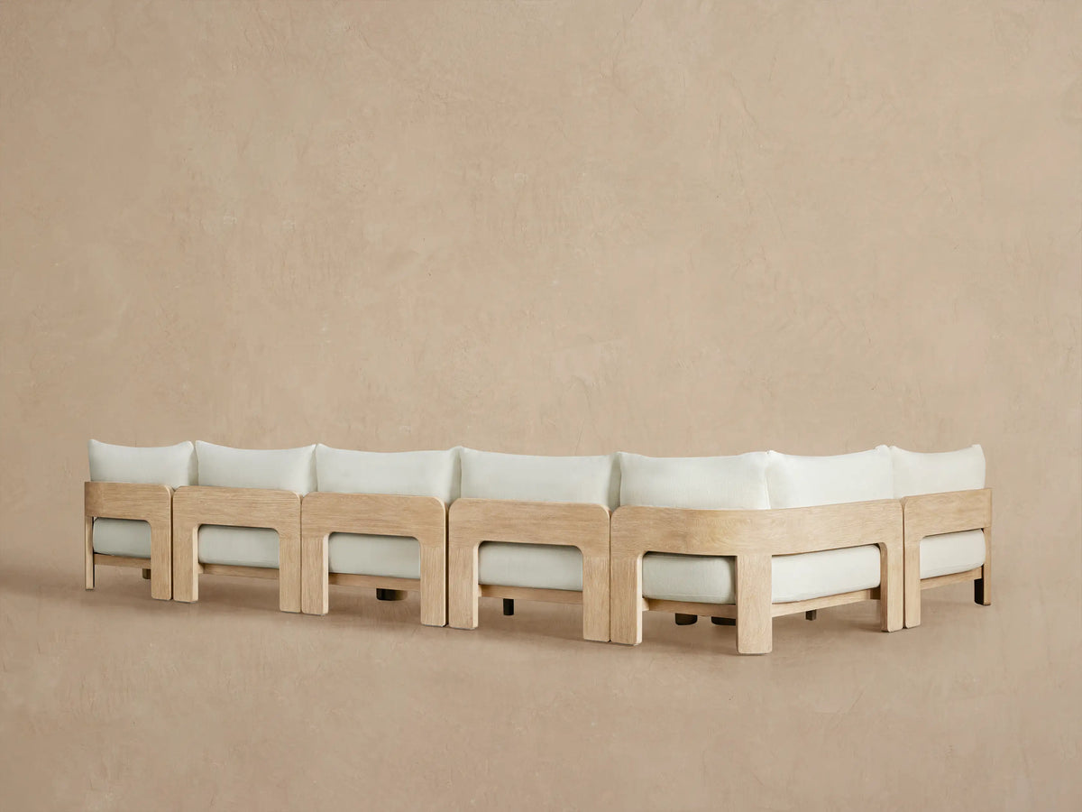 Close-up of Anami Outdoor Sectional's light teak armrest with distressed texture, embracing light cream cushions.