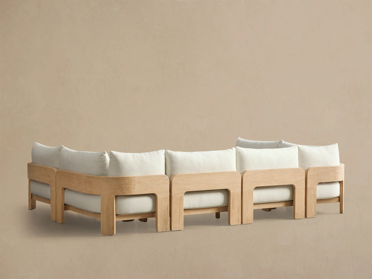 Close-up of the Anami Outdoor Three-Piece Sectional, showing a light teak wood frame with curved armrest and off-white cushions.