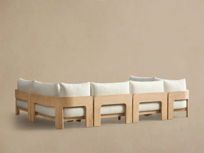 Close-up of the Anami Outdoor Three-Piece Sectional, showing a light teak wood frame with curved armrest and off-white cushions.