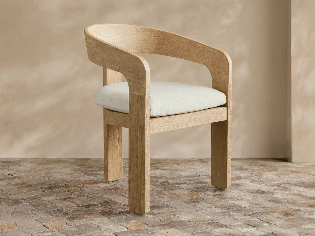 Anami Outdoor Dining Chair: light-toned, distressed teak wood with curved back and cream seat cushion on a tiled floor.