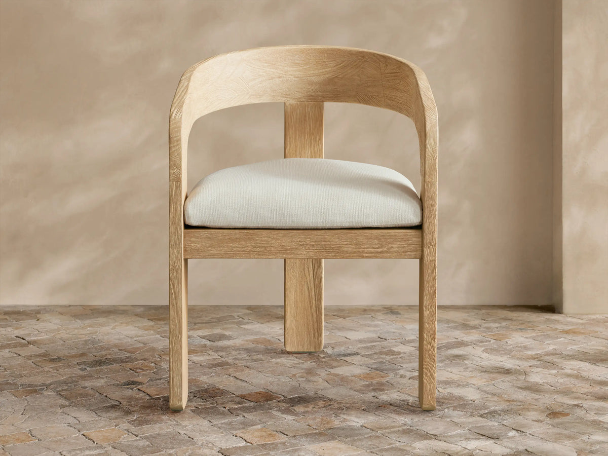 Anami Outdoor Dining Chair: light-toned, distressed teak wood with curved back and cream seat cushion on a tiled floor.