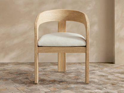 Anami Outdoor Dining Chair: light-toned, distressed teak wood with curved back and cream seat cushion on a tiled floor.