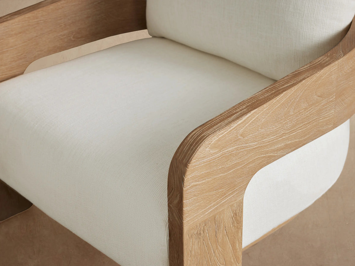 Anami Outdoor Lounge Chair, front view. Features light wooden frame with cream seat and back cushions on a tiled floor.