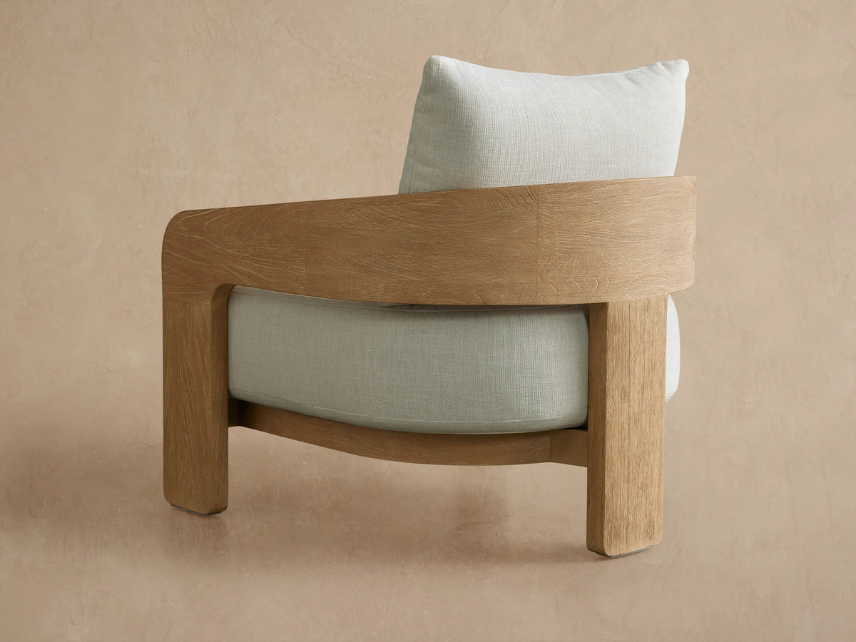 Close-up of Anami Outdoor Lounge Chair. Light teak wood frame with prominent grain and plush off-white textured cushions.