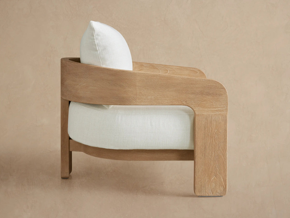 Anami Outdoor Lounge Chair with a curved light teak wood frame and pale green seat and back cushions, shown at an angle.