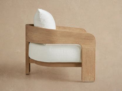 Anami Outdoor Lounge Chair with a curved light teak wood frame and pale green seat and back cushions, shown at an angle.