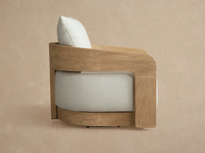 Anami Outdoor Swivel Chair, angled view. Light natural teak wood frame with light beige cushions against a tan background.