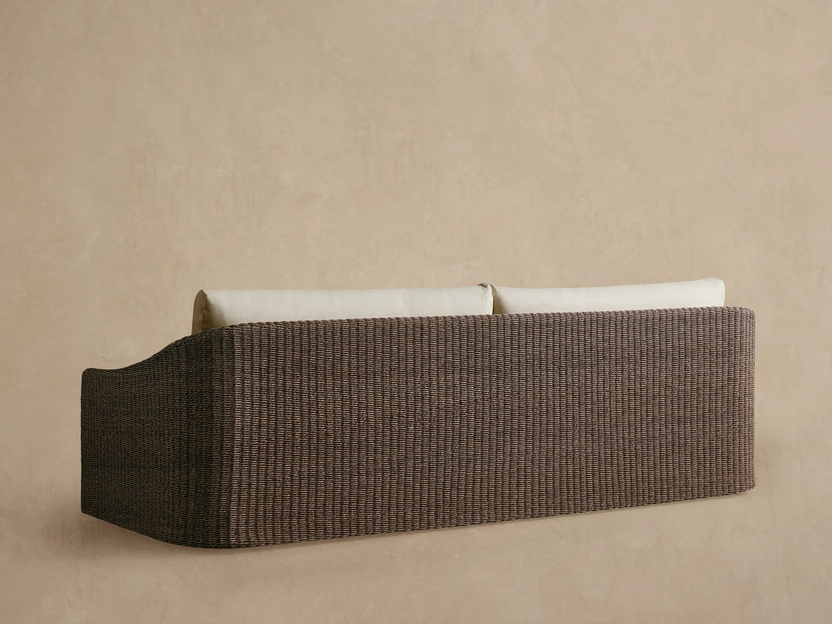 Close-up of Ancona Outdoor Sofa: dark brown handwoven wicker arm with a light beige, textured back cushion.