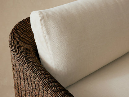Ancona Outdoor Sofa, front view, with dark brown woven wicker base and light cream cushions on a stone patio.