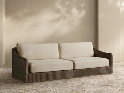 Ancona Outdoor Sofa with dark brown handwoven all-weather wicker frame and light beige cushions, set on a patio.