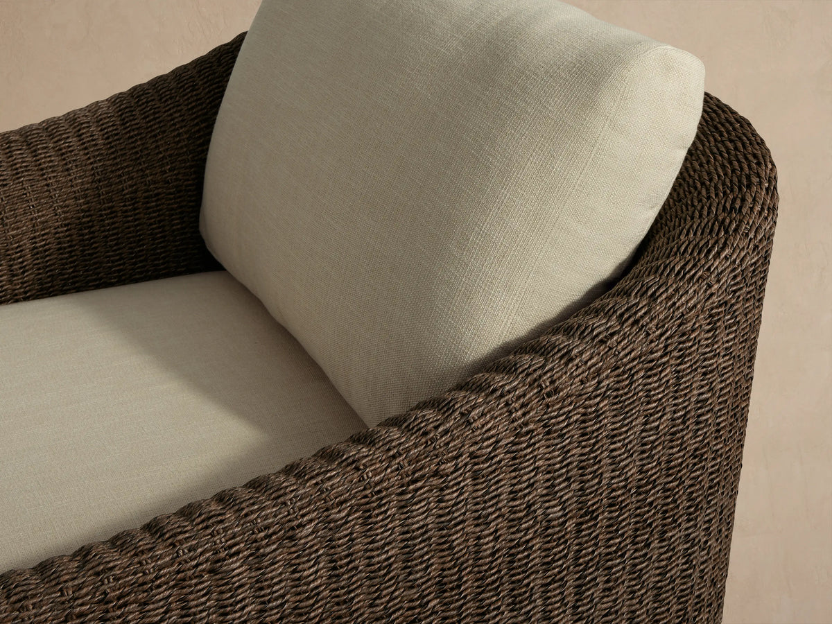 Front view of Ancona Outdoor Swivel Chair, featuring a dark brown handwoven wicker frame and light cream back and seat cushions.
