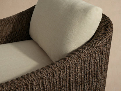 Front view of Ancona Outdoor Swivel Chair, featuring a dark brown handwoven wicker frame and light cream back and seat cushions.