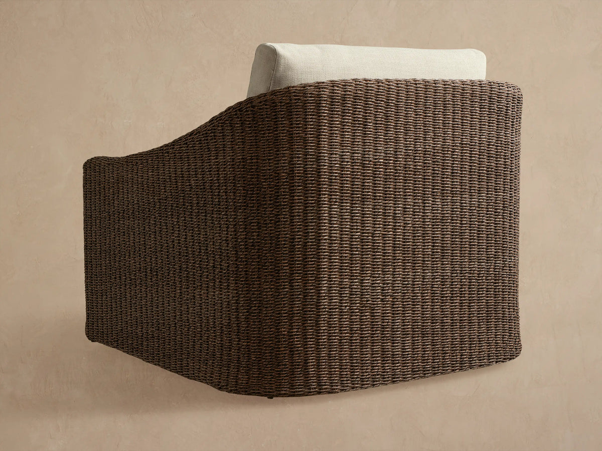 Ancona Outdoor Swivel Chair, side view, dark brown handwoven all-weather wicker with a light cream back cushion.