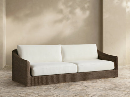 Ancona Outdoor Sofa, front view. Dark brown woven wicker frame, two large white seat and back cushions on a tiled patio.