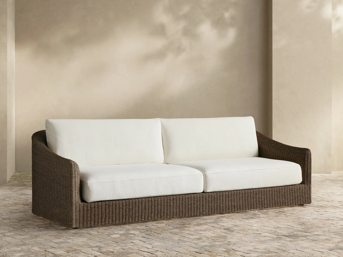 Ancona Outdoor Sofa: dark brown handwoven wicker frame with two white seat and back cushions, on a tiled outdoor patio.