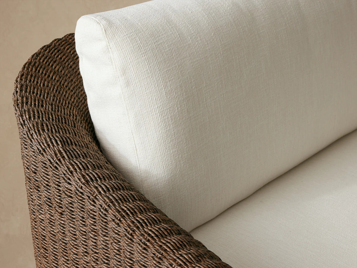 Ancona Outdoor Sofa: dark brown woven wicker frame, white seat and back cushions, shown on a stone patio.