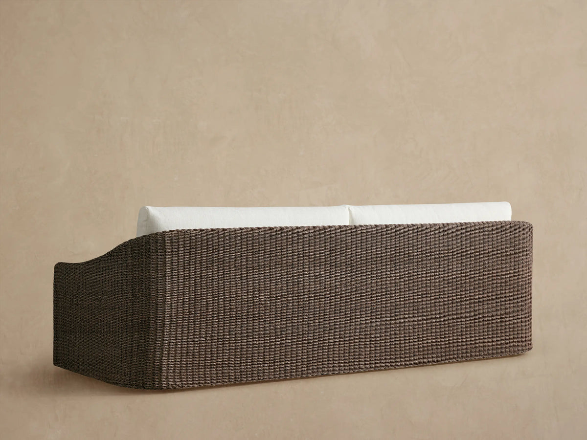 Close-up of Ancona Outdoor Sofa arm & back cushion. Brown handwoven wicker frame with a light, textured fabric cushion.