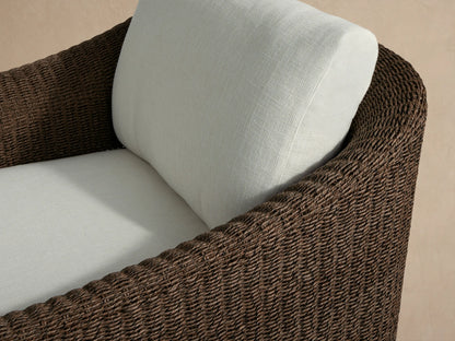 Ancona Outdoor Swivel Chair, front view, dark brown woven wicker frame & light cream cushions on a stone patio.