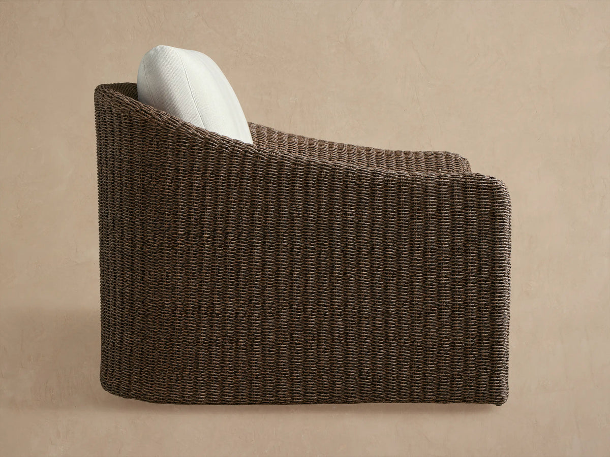 Ancona Outdoor Swivel Chair. Dark brown woven wicker, light cream cushion, seen from the back against a beige wall.