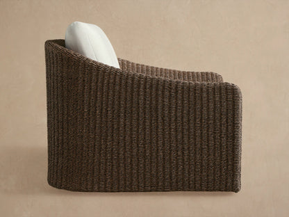 Ancona Outdoor Swivel Chair. Dark brown woven wicker, light cream cushion, seen from the back against a beige wall.