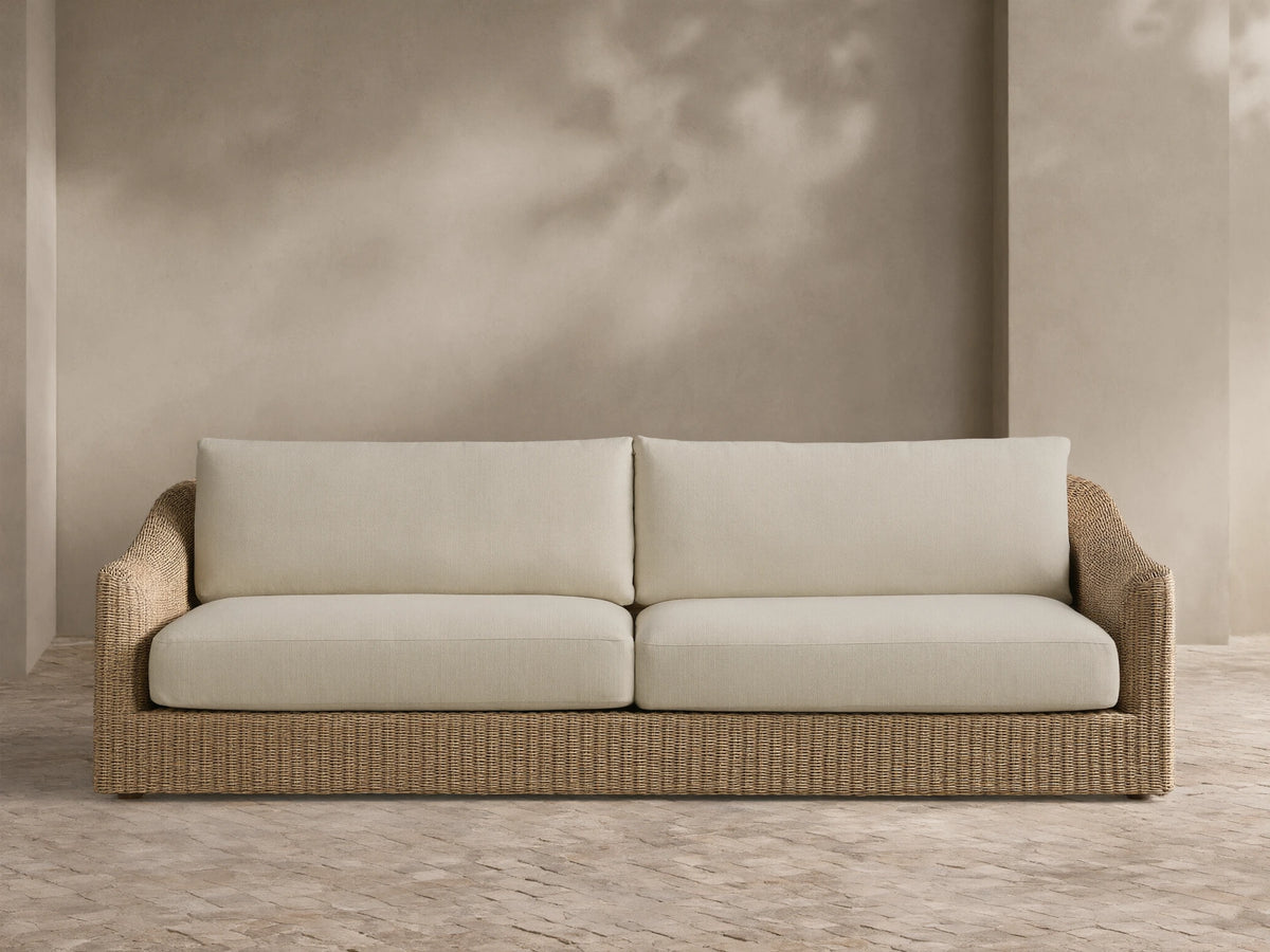 Front view of the Ancona Outdoor Sofa with natural-toned woven wicker and cream cushions.